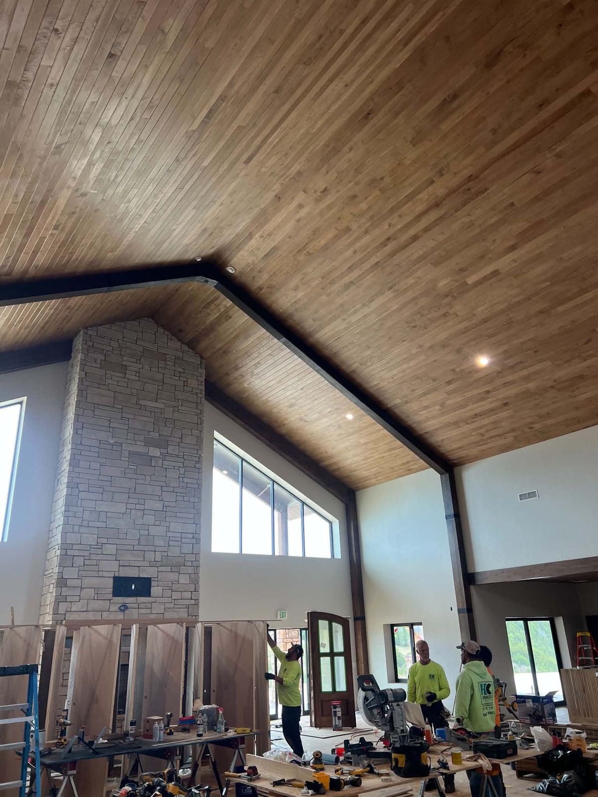 After: the same great room with a finished wood plank ceiling, stone chimney and black steel beam